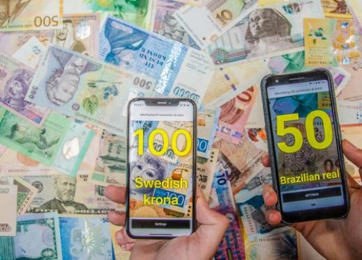 Smart phones identifying 100 Swedish krona and 50 Brazilian real; background of numerous bank notes from different countries.