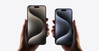 Two models, iPhone 15 Pro Max, iPhone 15 Pro, a hand holds each model, iPhone 15 Pro Max is taller and wider in the hand than iPhone 15 Pro, all screen display, Dynamic Island centered near top, rounded corners.  
