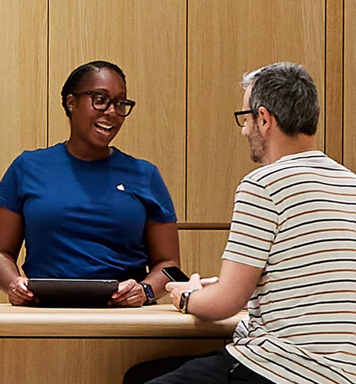 Two Genius Bar technicians provide one-on-one support to customers in a sleek, wood-paneled Apple Store
